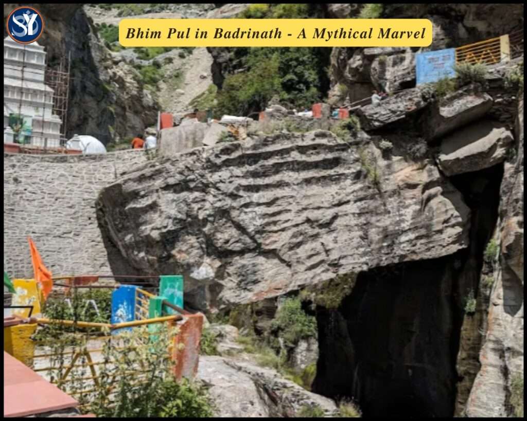 A natural stone bridge known as Bhim Pul spans the gushing Saraswati River amid steep cliffs and lush greenery near Badrinath, with the Himalayas rising in the background.