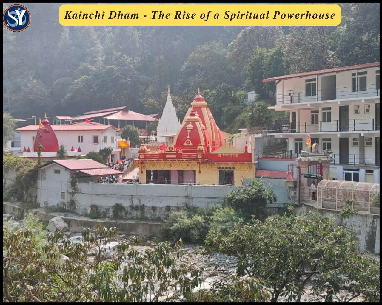 A peaceful view of Kainchi Dham Ashram nestled in the green hills of Uttarakhand, surrounded by pine forests and the flowing Kosi River, with devotees walking calmly in a serene spiritual setting.